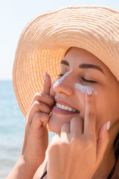 Smiling woman in hat is applying sunscreen on her face. Indian style.
